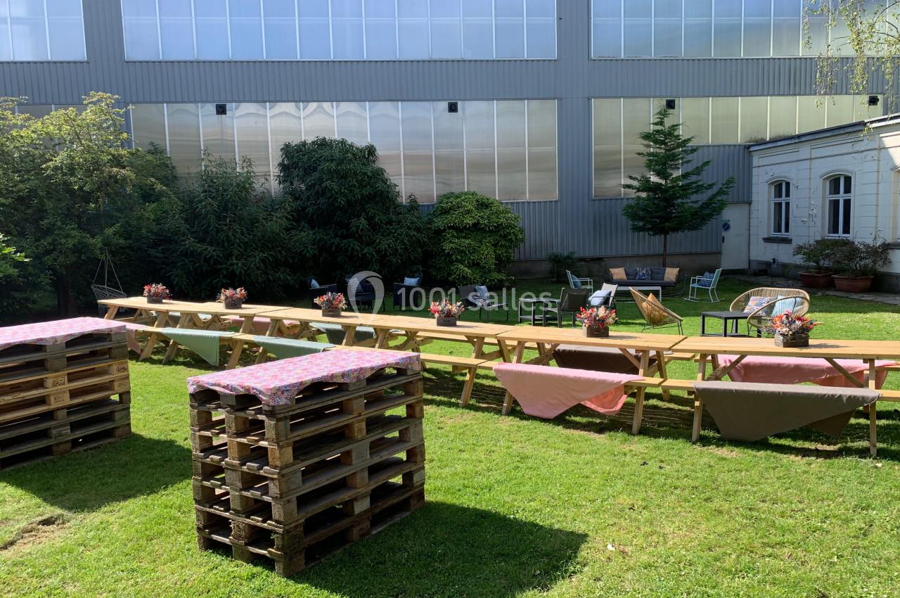 Tables en bois décorées de nappes et de bouquets, disposées sur une pelouse devant un bâtiment industriel.