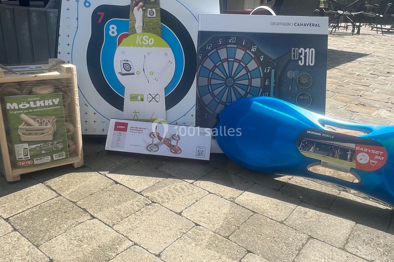Des jeux et équipements de loisirs, dont une cible, un jeu de fléchettes, et un jeu de quilles, posés sur un sol pavé.