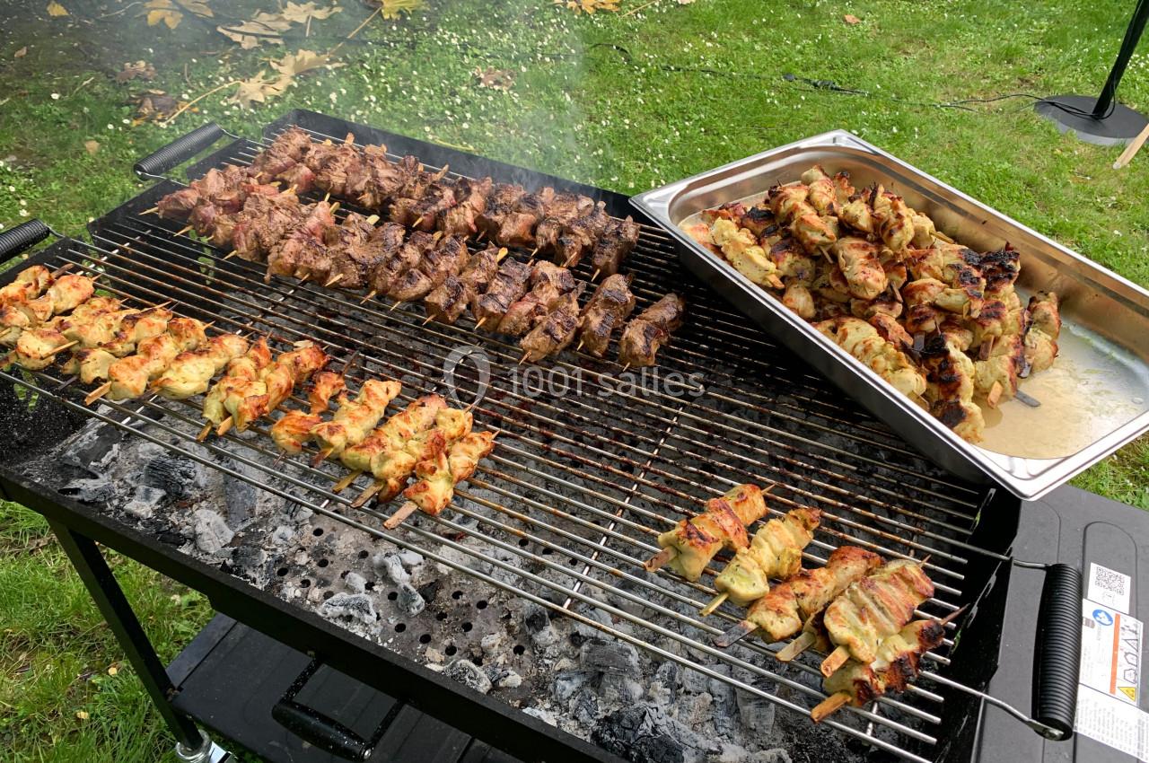 Brochettes de viande et de poulet grillées sur un barbecue, avec un plateau contenant des brochettes cuites à côté.