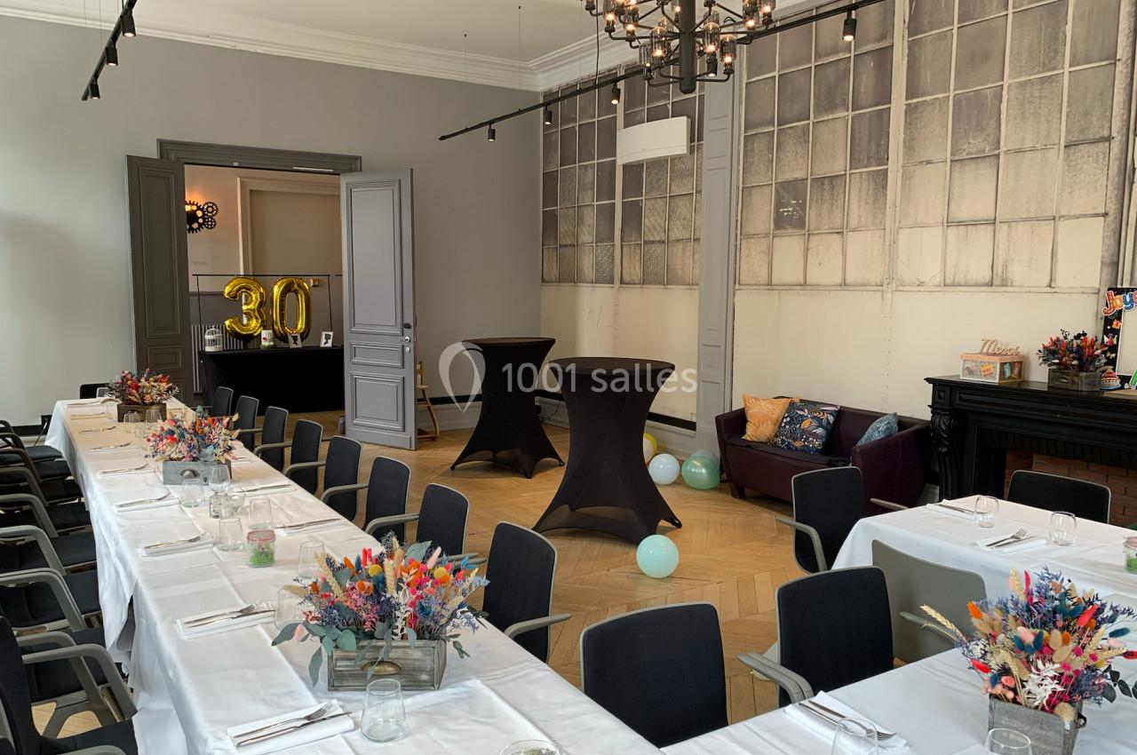 Salle décorée pour un événement avec tables dressées, bouquets colorés, ballons et chiffre ’30’ en ballon doré.