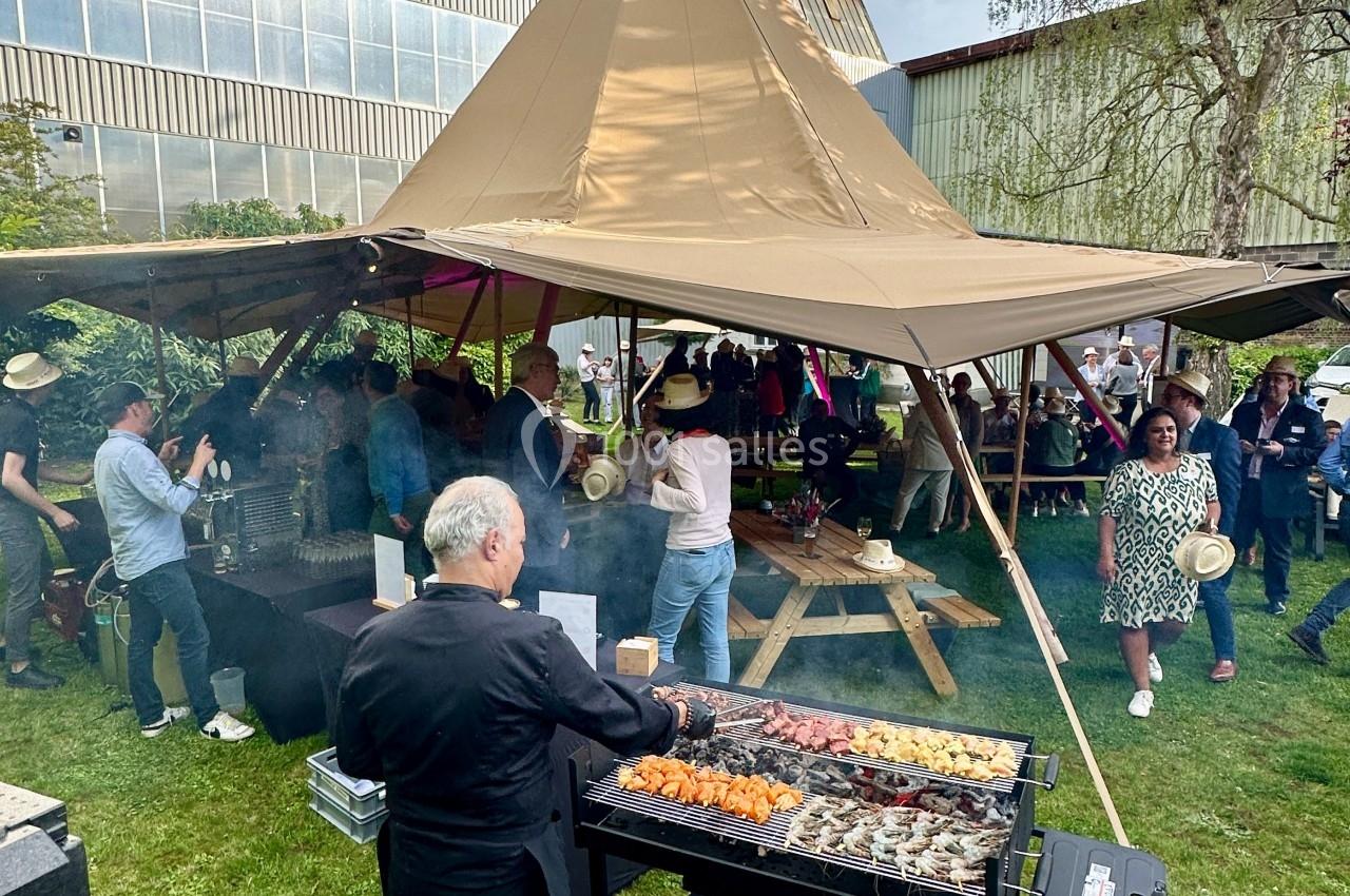 Un cuisinier prépare des brochettes sur un barbecue lors d'un événement en plein air sous une tente tipi.