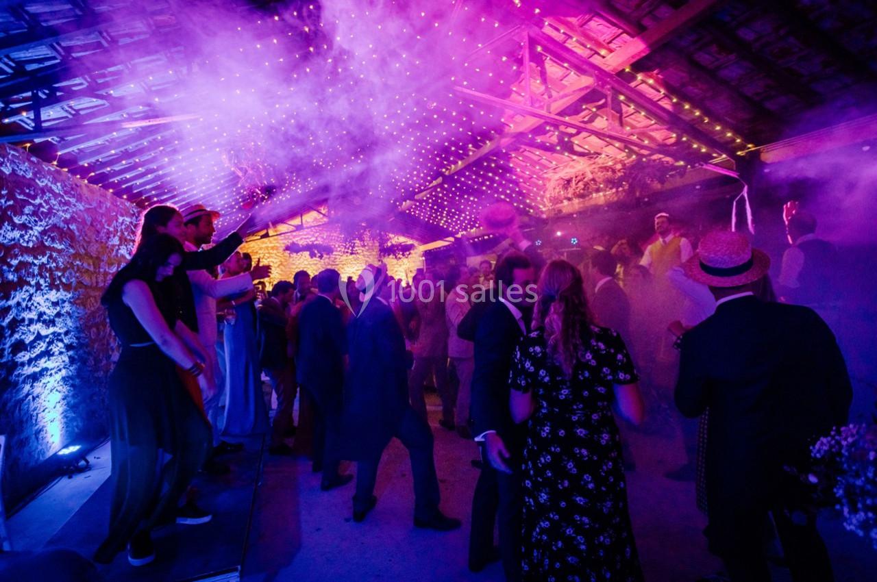 Personnes dansant sous des lumières violettes et une ambiance festive dans une salle avec un toit en bois apparent.