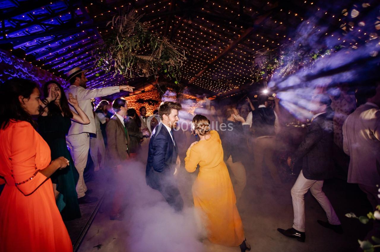 Des personnes dansent sous des lumières colorées et une ambiance festive dans une salle décorée avec des guirlandes…