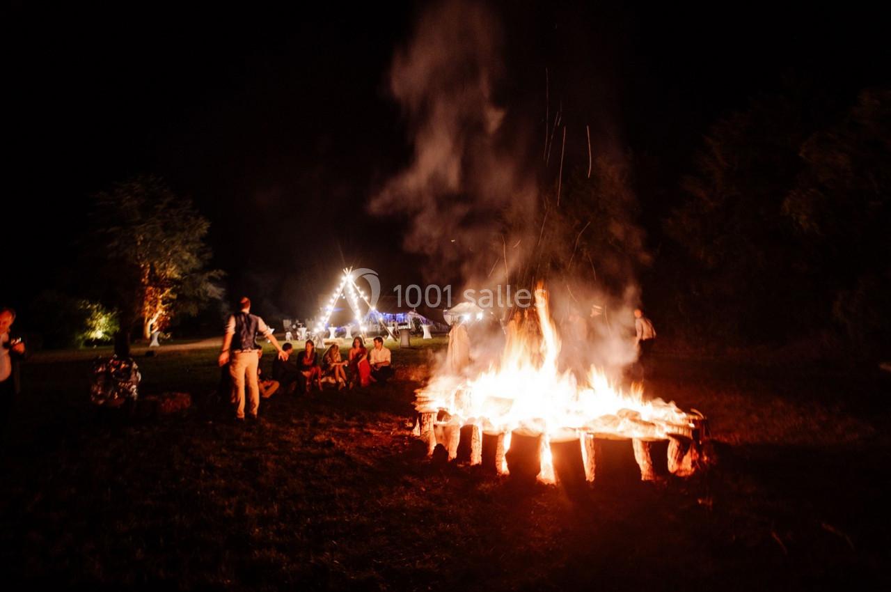 Un groupe de personnes assises autour d'un grand feu de camp dans un espace extérieur éclairé la nuit.