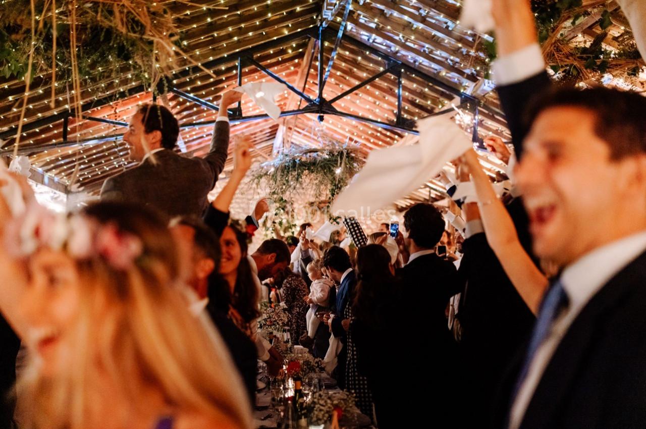 Des invités célèbrent joyeusement dans une salle décorée, agitant des serviettes blanches au-dessus de leurs têtes.