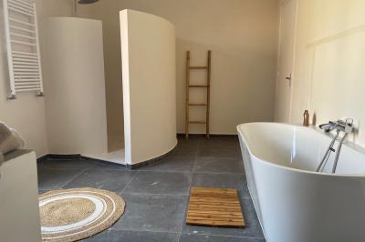 Salle de bain lumineuse avec baignoire moderne, échelle en bois, miroir incliné et double vasque sur meuble blanc.