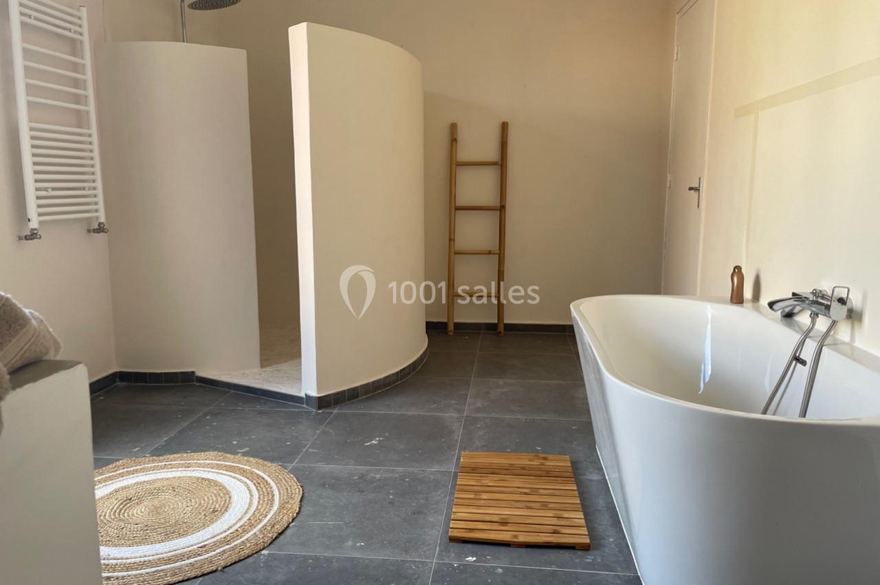 Salle de bain moderne avec douche ouverte, baignoire blanche, tapis rond en jute et échelle en bois décorative.