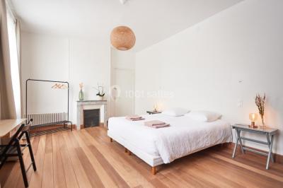 Salle de bain lumineuse avec baignoire moderne, échelle en bois, miroir incliné et double vasque sur meuble blanc.