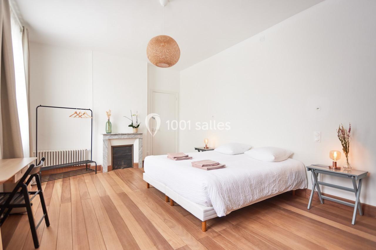 Chambre lumineuse avec lit double, parquet en bois, cheminée décorative et mobilier minimaliste.