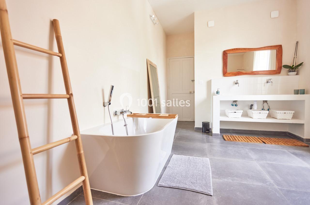 Salle de bain lumineuse avec baignoire moderne, échelle en bois, miroir incliné et double vasque sur meuble blanc.