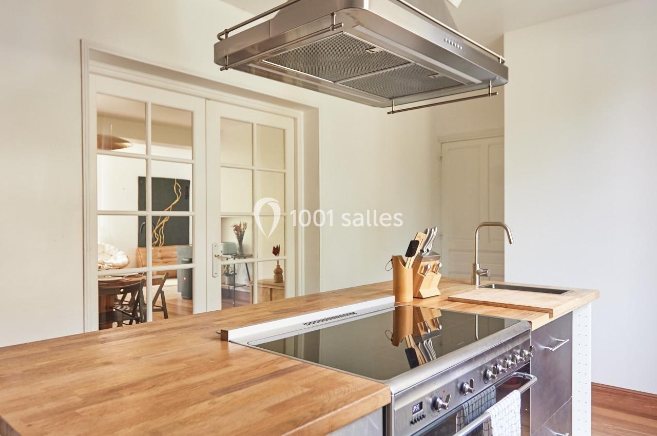 Cuisine moderne avec îlot central en bois, plaque de cuisson intégrée, hotte suspendue et vue sur une salle à manger.
