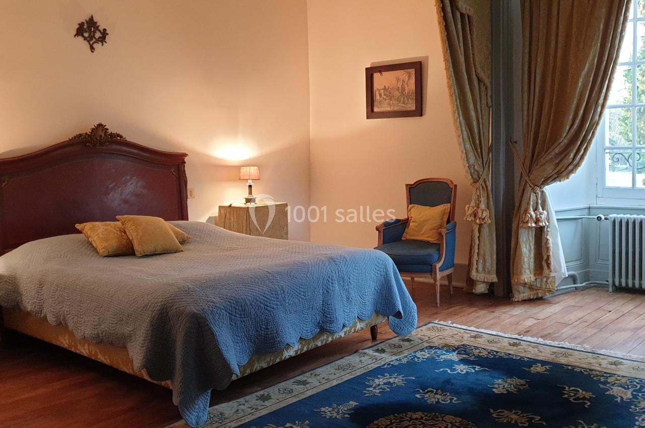 Location salle Assay (Indre-et-Loire) - Chateau de Basché #10 Chambre lumineuse avec lit double, fauteuil, tapis bleu, rideaux dorés et grande fenêtre donnant sur un jardin.
