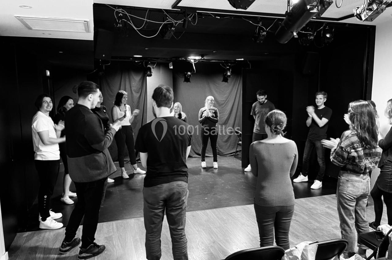 Un groupe de personnes en cercle dans une salle de théâtre, applaudissant et participant à une activité collective.