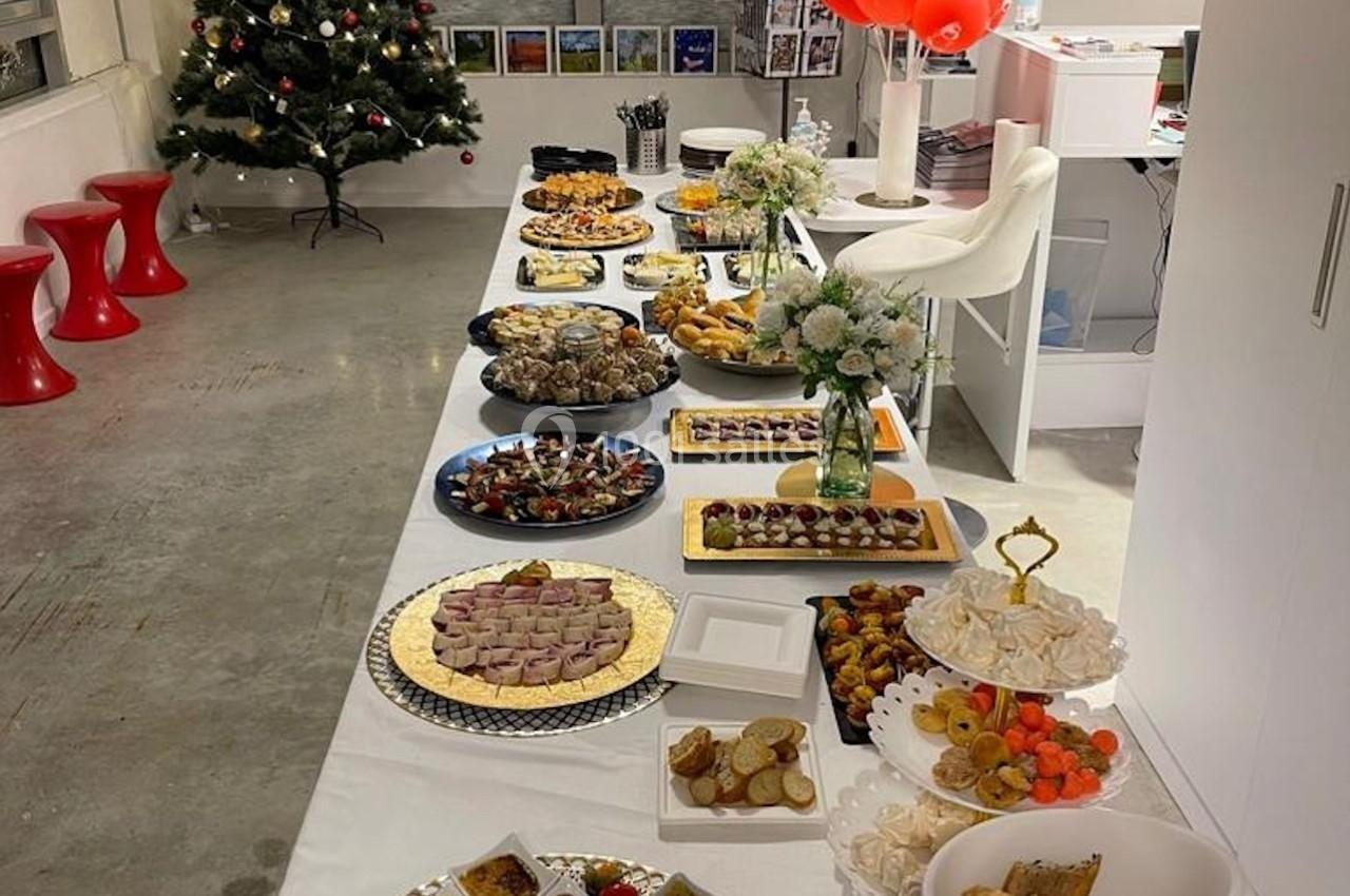 Table garnie de divers plats et desserts dans une salle décorée avec un sapin de Noël et des ballons rouges.