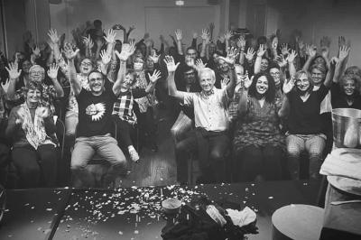 Tables dressées avec nappes, bouteilles, verres et un bouquet de fleurs dans une salle lumineuse avec de grandes fenêtres.