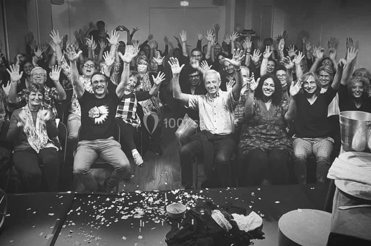 Un groupe de personnes assises dans une salle, levant les bras et souriant face à la caméra.