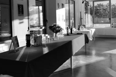 Tables dressées avec nappes, bouteilles, verres et un bouquet de fleurs dans une salle lumineuse avec de grandes fenêtres.