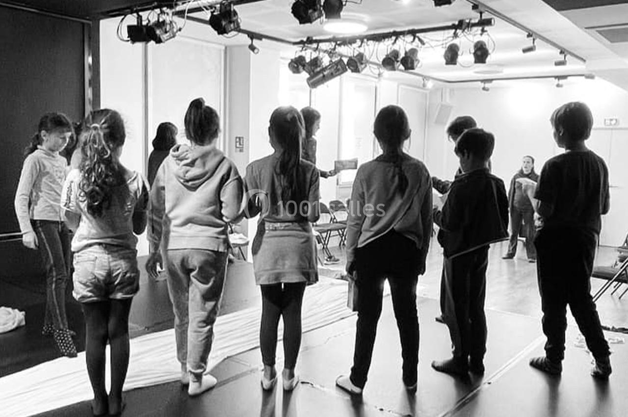 Des enfants debout sur une scène, vus de dos, participent à une activité dans une salle éclairée.