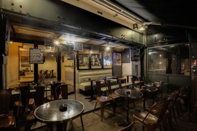 Verres de cocktails variés, dont des shots avec citrons verts et des spritz orange, posés sur des tables en bois.