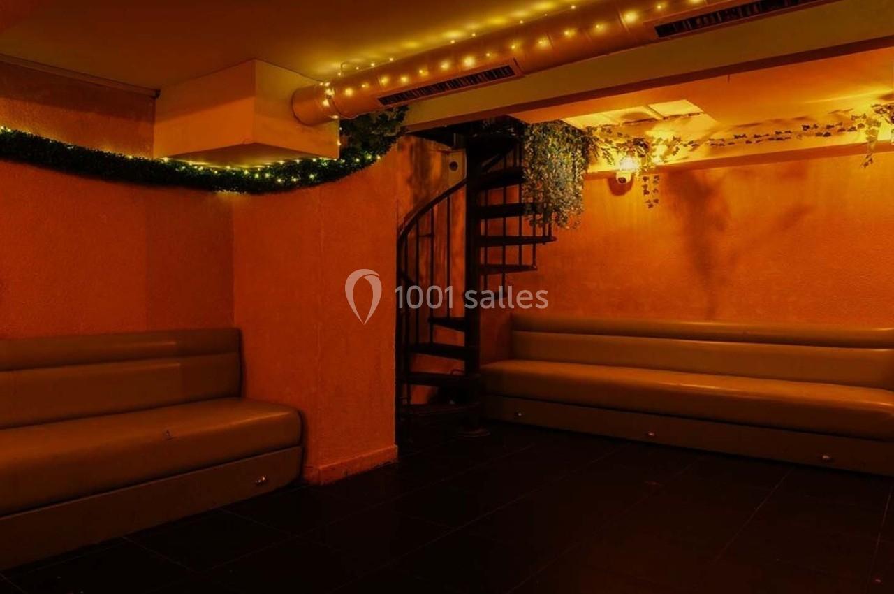 Salle avec des banquettes, un escalier en colimaçon, éclairage tamisé et décorations lumineuses et végétales.