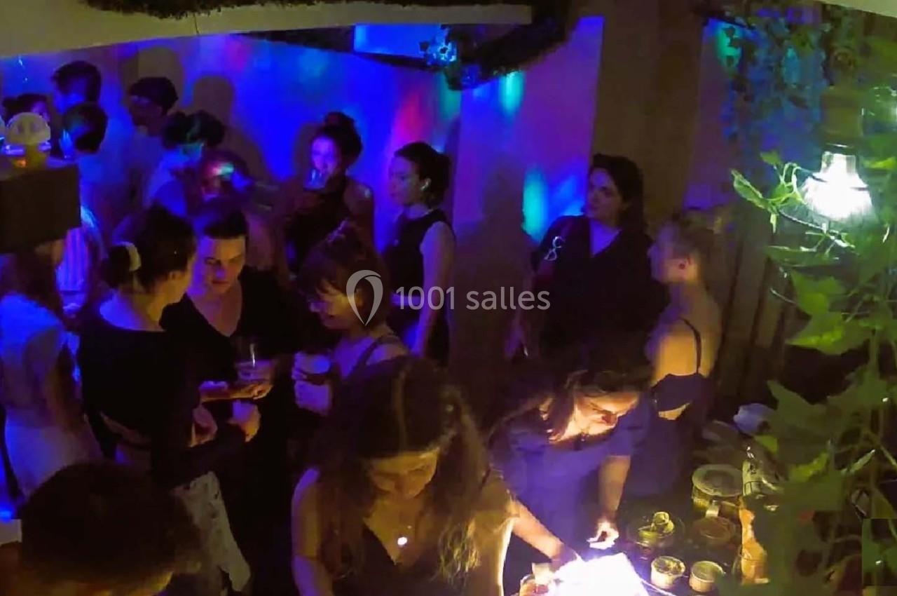 Groupe de personnes discutant et partageant des boissons dans une pièce éclairée par des lumières colorées.