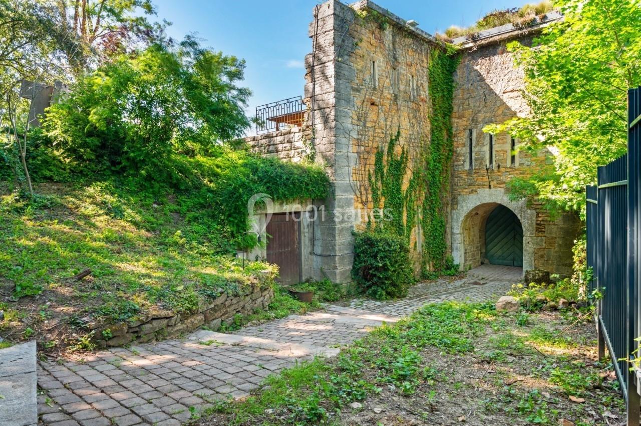 Entrée voûtée d'un bâtiment en pierre ancienne, entourée de végétation et d'un chemin pavé.