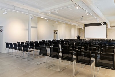 Tables rondes dressées avec nappes noires, serviettes pliées et verres dans une salle lumineuse avec grandes fenêtres.