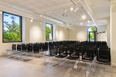 Tables rondes dressées avec nappes noires, serviettes pliées et verres dans une salle lumineuse avec grandes fenêtres.