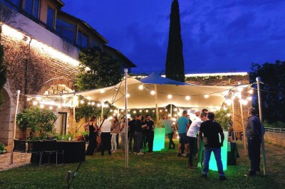 Tables rondes dressées avec nappes noires, serviettes pliées et verres dans une salle lumineuse avec grandes fenêtres.