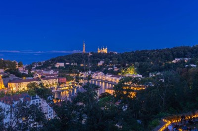 Tables rondes dressées avec nappes noires, serviettes pliées et verres dans une salle lumineuse avec grandes fenêtres.