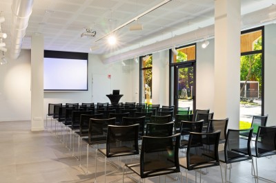 Tables rondes dressées avec nappes noires, serviettes pliées et verres dans une salle lumineuse avec grandes fenêtres.