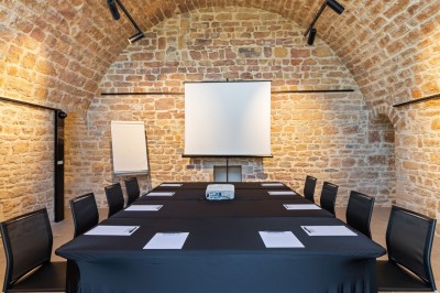 Tables rondes dressées avec nappes noires, serviettes pliées et verres dans une salle lumineuse avec grandes fenêtres.