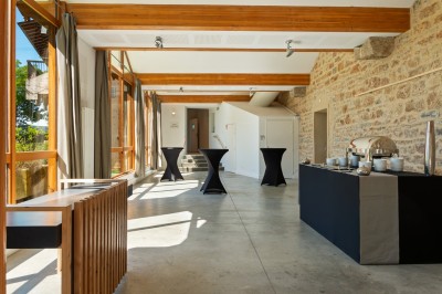 Tables rondes dressées avec nappes noires, serviettes pliées et verres dans une salle lumineuse avec grandes fenêtres.