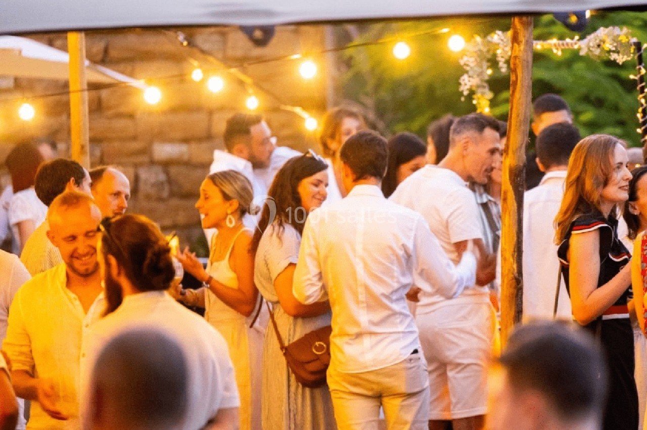 Groupe de personnes discutant et partageant un moment convivial lors d'un événement en extérieur, éclairé par des guirlandes…