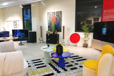 Tables rondes dressées avec nappes noires, serviettes pliées et verres dans une salle lumineuse avec grandes fenêtres.