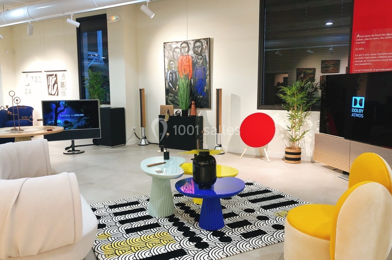 Salle d'exposition moderne avec mobilier design, œuvres d'art accrochées et équipements audiovisuels.