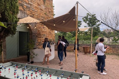 Tables rondes dressées avec nappes noires, serviettes pliées et verres dans une salle lumineuse avec grandes fenêtres.