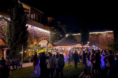 Tables rondes dressées avec nappes noires, serviettes pliées et verres dans une salle lumineuse avec grandes fenêtres.