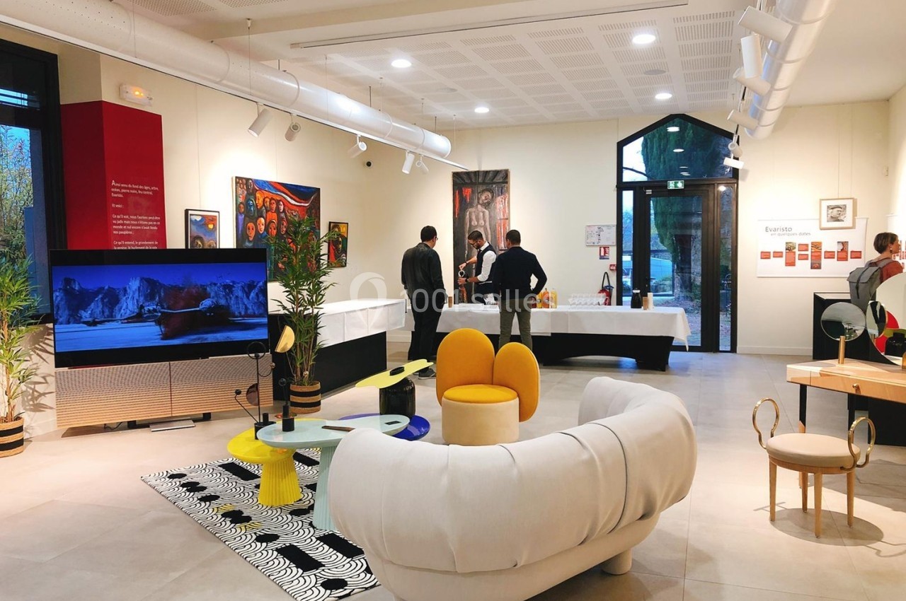 Espace intérieur lumineux avec mobilier design, œuvres d'art exposées et personnes discutant près d'une table.