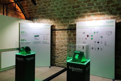 Tables rondes dressées avec nappes noires, serviettes pliées et verres dans une salle lumineuse avec grandes fenêtres.