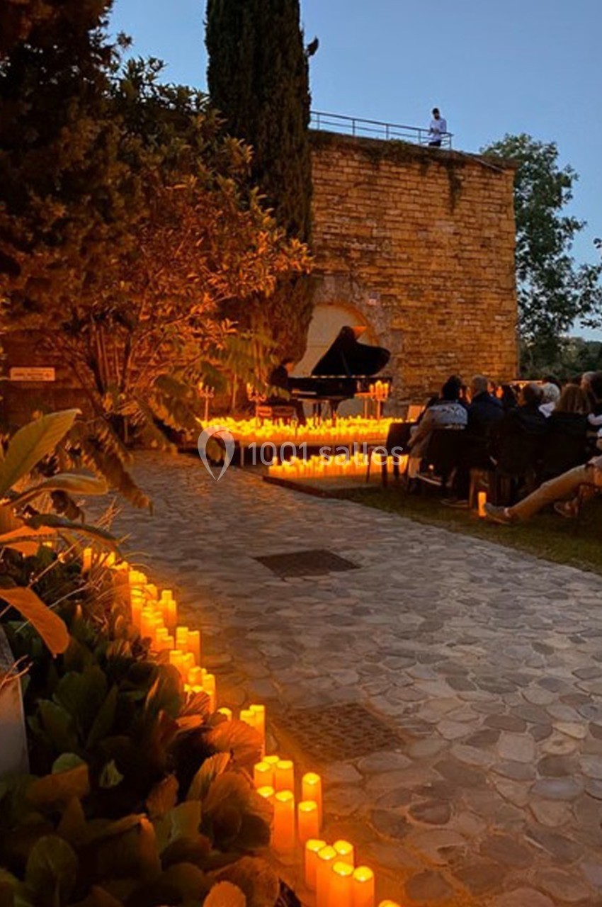 Allée pavée bordée de bougies menant à un piano en plein air, entouré de spectateurs au crépuscule.