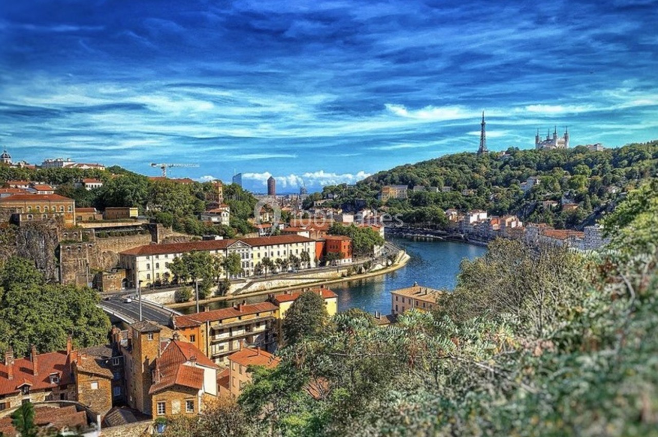 Vue panoramique d'une ville avec des bâtiments en briques, une rivière sinueuse et des collines verdoyantes sous un ciel…