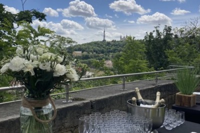 Tables rondes dressées avec nappes noires, serviettes pliées et verres dans une salle lumineuse avec grandes fenêtres.