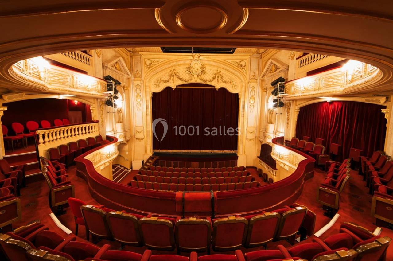 Intérieur d'un théâtre avec des sièges rouges, une scène centrale avec rideau fermé et une architecture ornée.