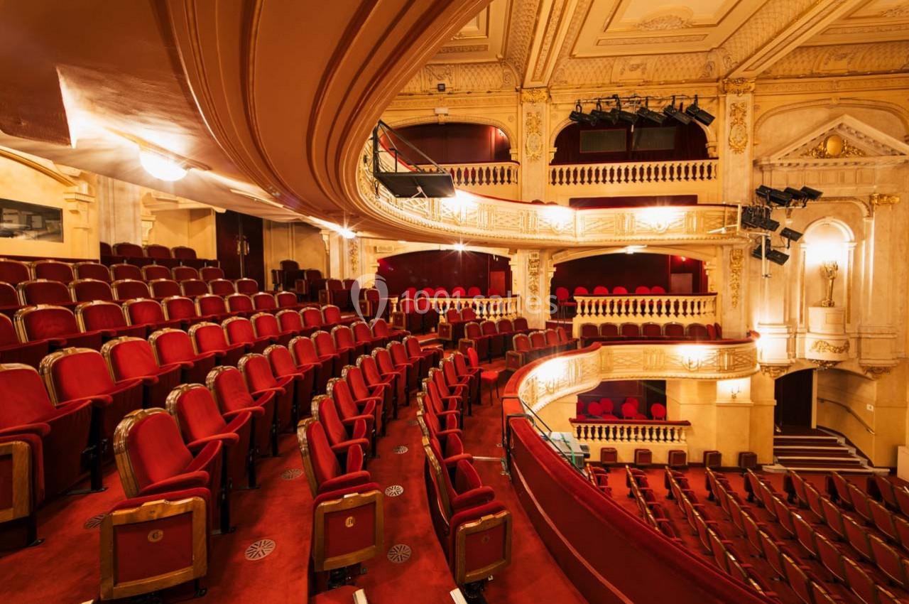 Salle de théâtre avec des rangées de sièges rouges, balcons ornés et décorations architecturales élégantes.