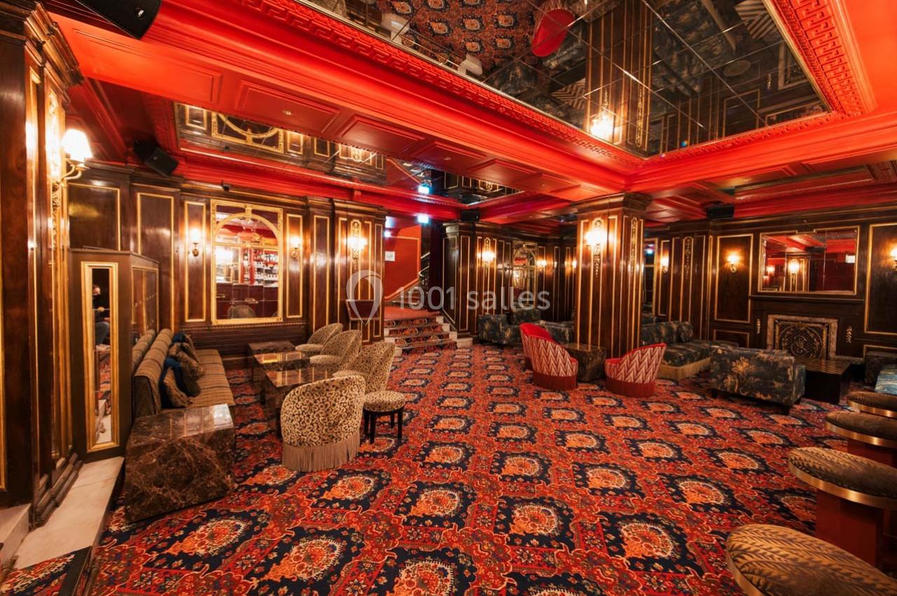Intérieur d'un salon luxueux avec tapis rouge à motifs, fauteuils variés et murs ornés de boiseries dorées.