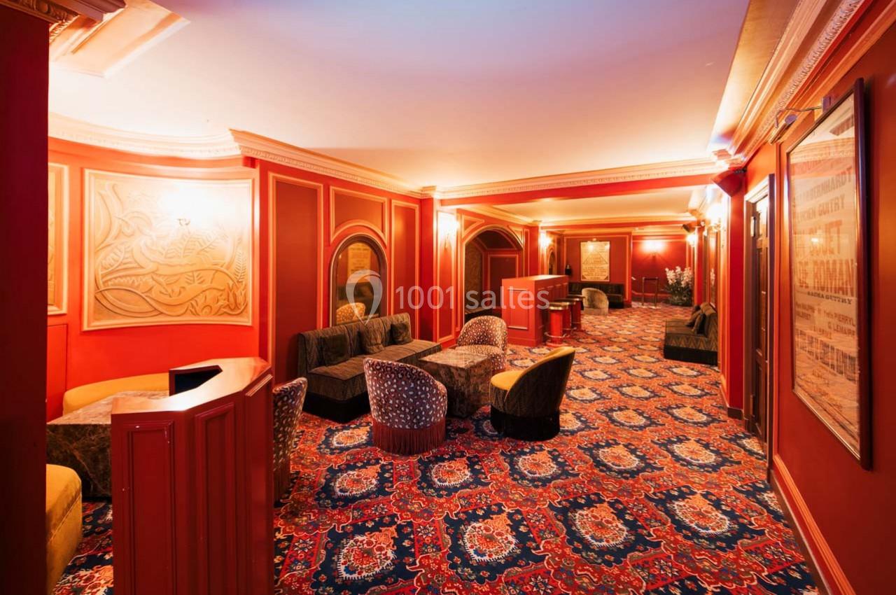 Salon d'attente avec fauteuils, tables basses, murs rouges et tapis à motifs dans un décor élégant et chaleureux.