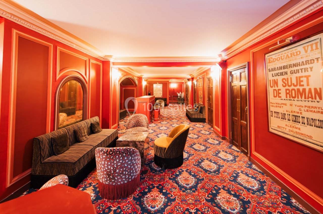 Salon élégant avec fauteuils colorés, canapé, tapis à motifs et affiches encadrées sur des murs rouges.