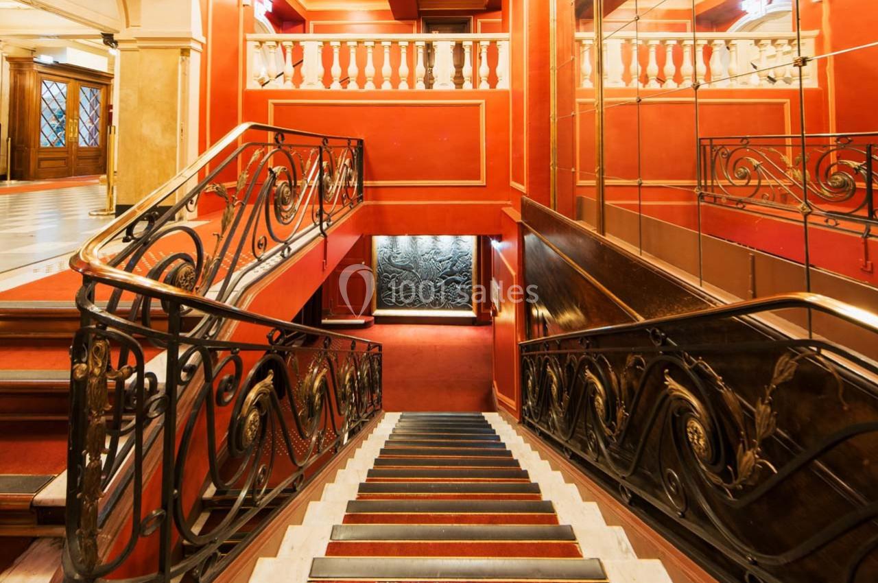 Escalier intérieur élégant avec rambardes en fer forgé, murs rouges et miroir reflétant l'espace.