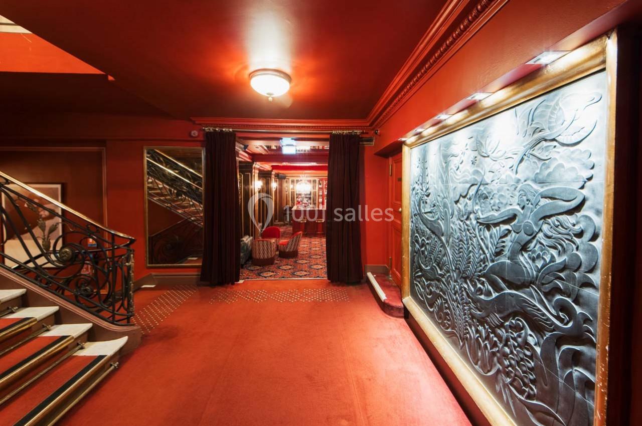 Escalier et couloir décoré de rouge avec fresque murale sculptée, éclairage chaleureux et moquette au sol.